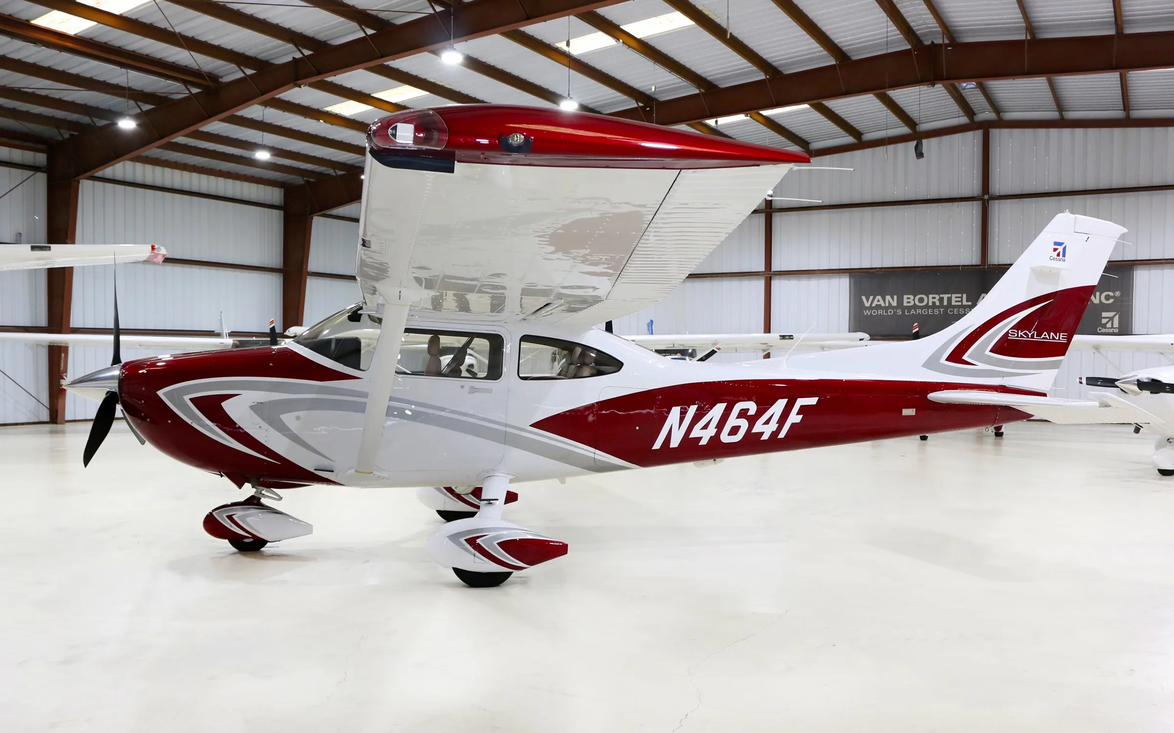 A red and white Cessna Skylane aircraft, registration N464F, is parked inside a hangar.