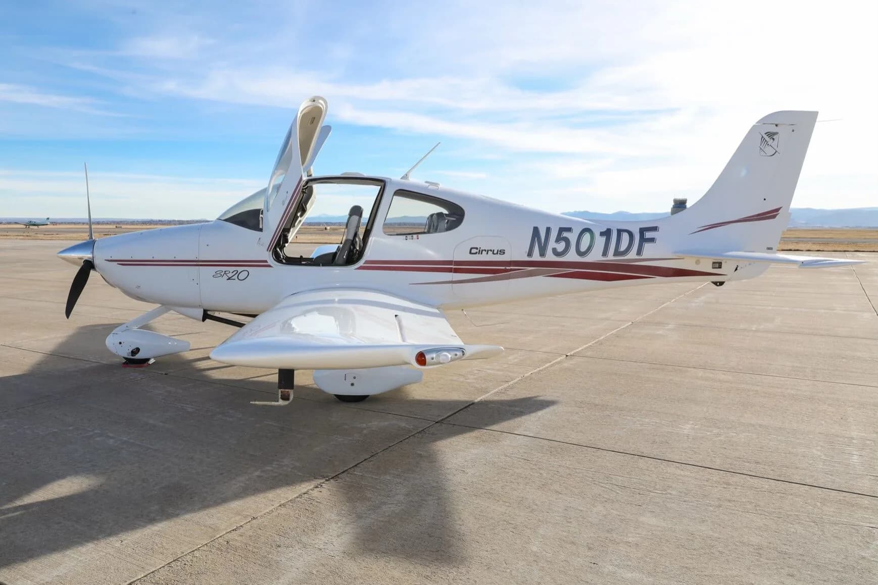 A white Cirrus SR20 aircraft with red stripes, tail number N501DF, parked on an airfield with its gull-wing doors open.