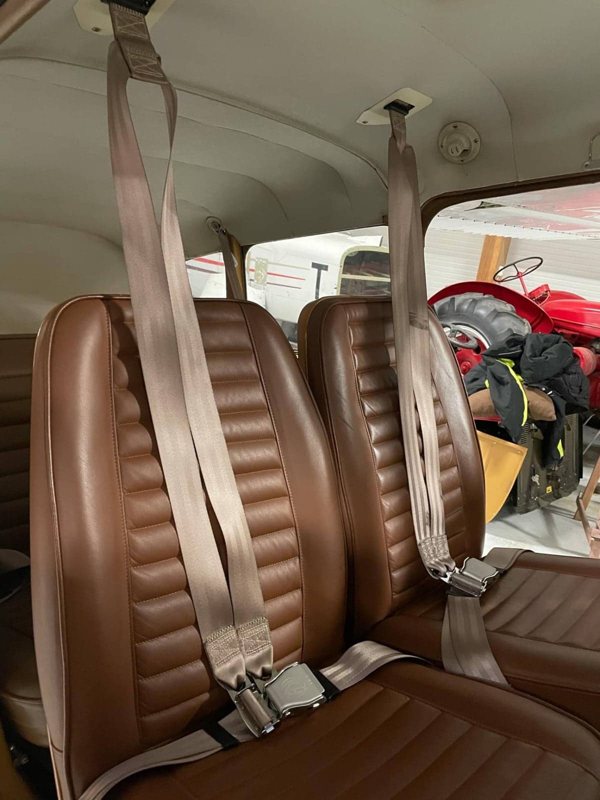 Brown leather aircraft seats with seatbelts, viewed from inside the cabin looking forward.