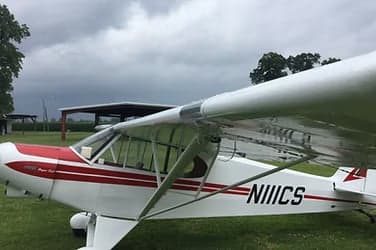 A white and red Piper Super Cub parked on a grassy field.