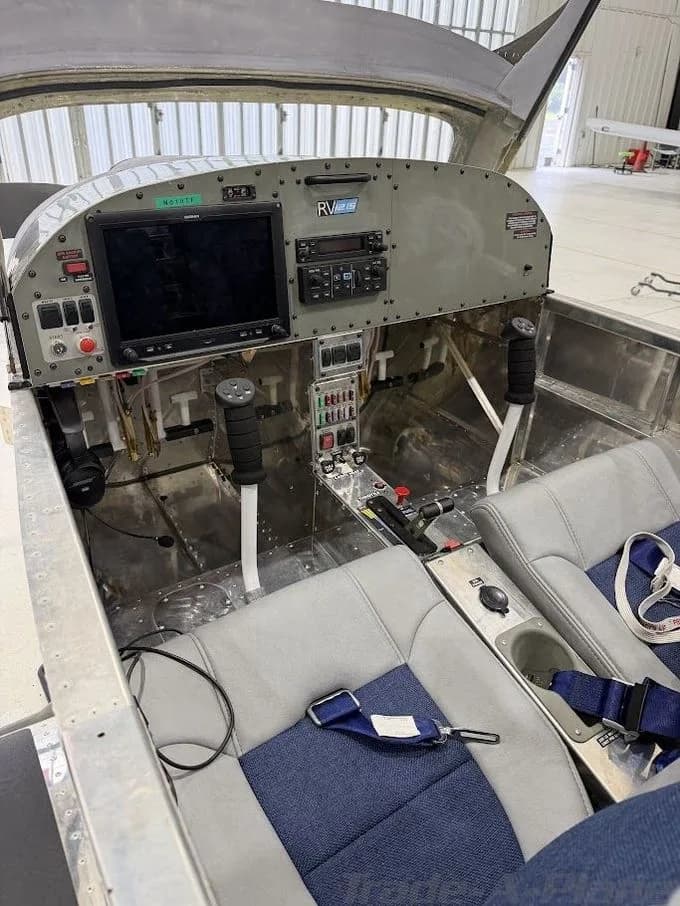 The cockpit of an RV-12S light aircraft, featuring a Garmin glass panel, side-stick controls, and blue and grey seats, inside a hangar.