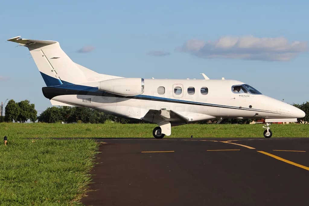 A white Embraer Phenom 100 with blue and black stripes on a runway under a clear sky.