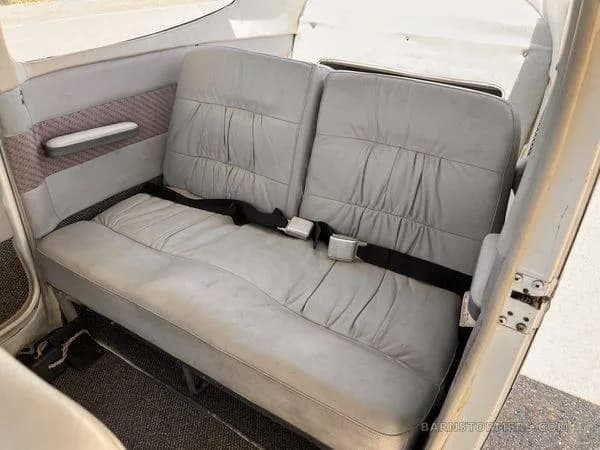 The light gray leather rear bench seat of a small aircraft cabin with seatbelts, viewed from the side.