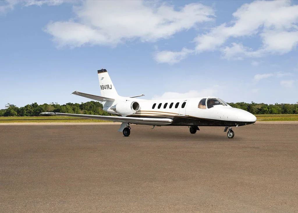 A white and black Cessna Citation business jet N941RJ with gold stripes is parked on a tarmac under a partly cloudy sky, viewed from the front-right.
