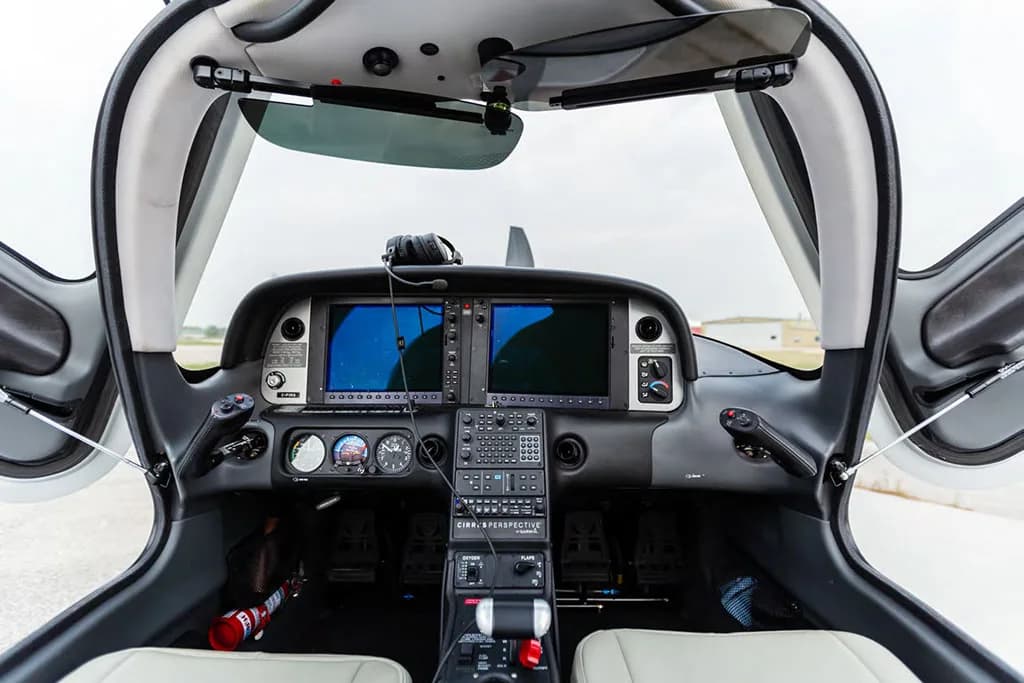 A detailed view of the modern glass cockpit of a Cirrus aircraft with dual screens and side yokes, seen with the doors open.