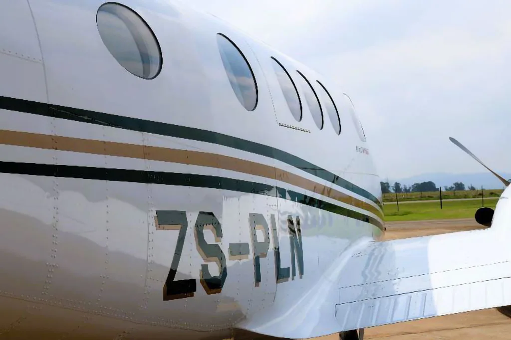 A close-up of the white fuselage of a Beechcraft King Air C90GTx, showing the windows and registration ZS-PLN.
