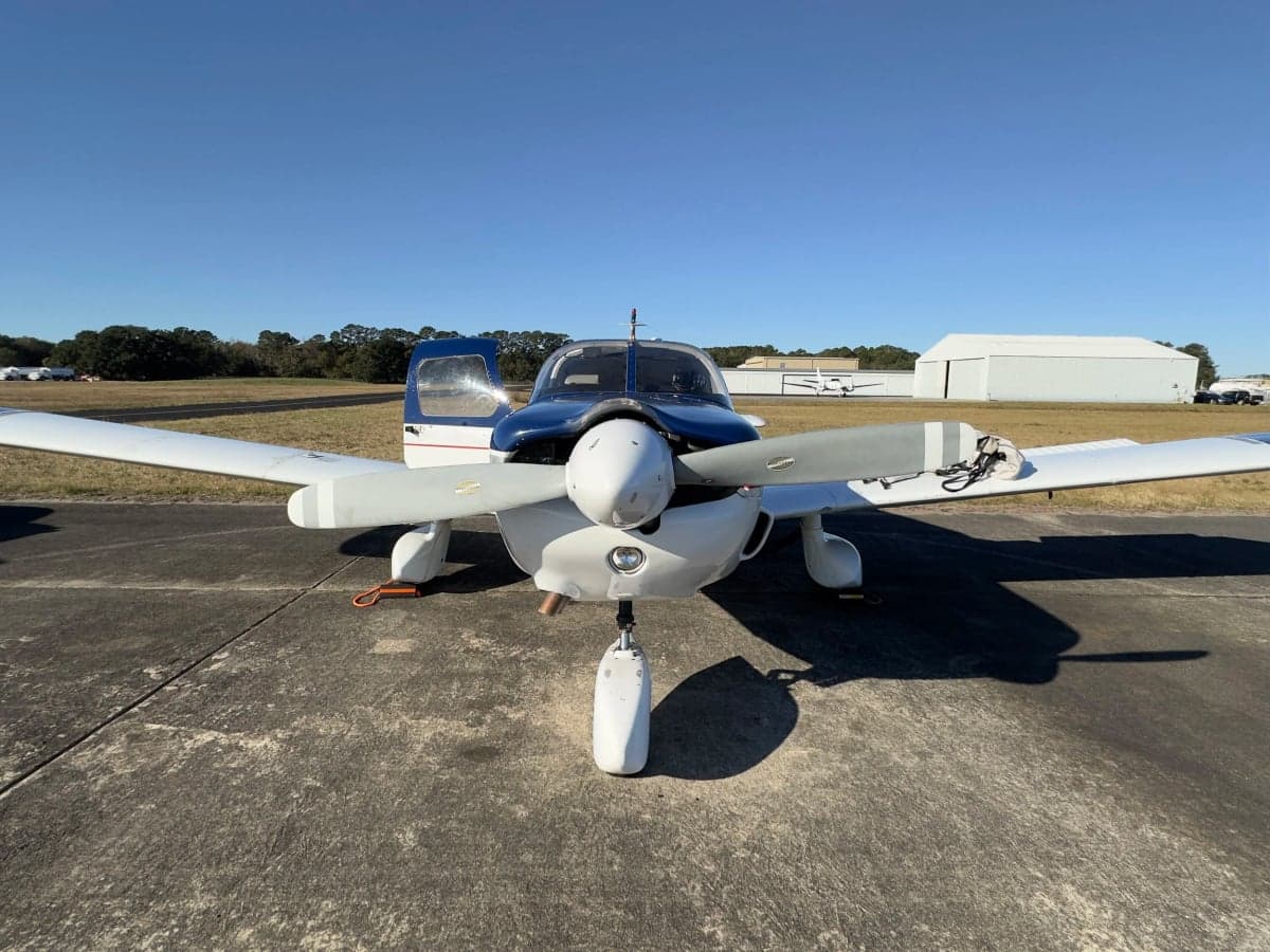 Front view of a blue and white Piper Cherokee aircraft on the ground.