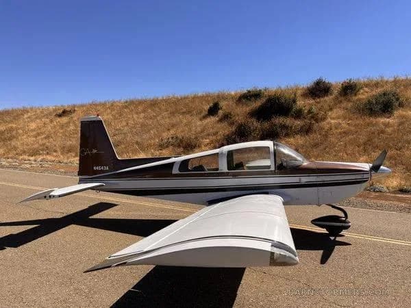 A side view of a brown and white Grumman American AA-5 Traveler aircraft (N4543A) parked on an asphalt surface with a grassy hill in the background.