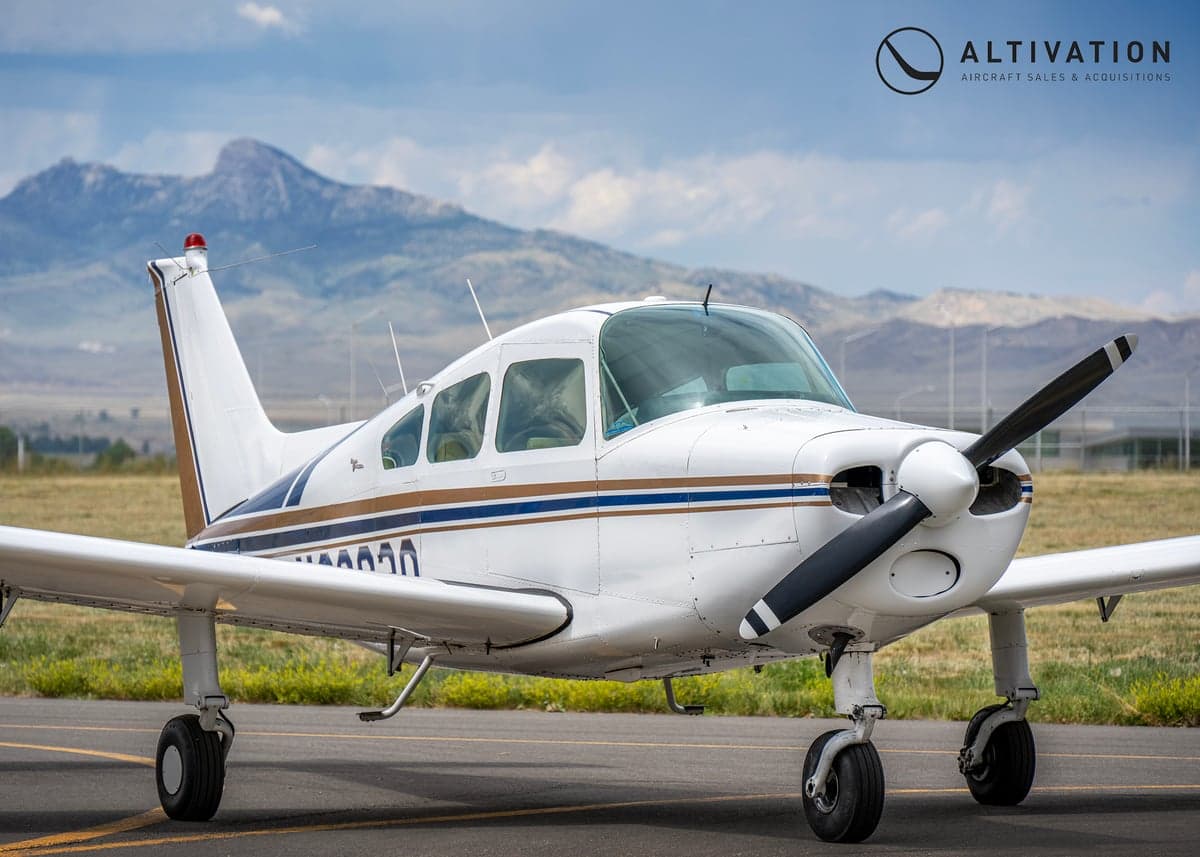 Close up of the front of a white and blue Piper aircraft on the tarmac.