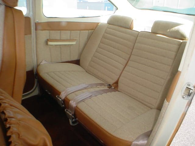 The rear bench seat of a small aircraft cabin, upholstered in tan and brown fabric with seatbelts.