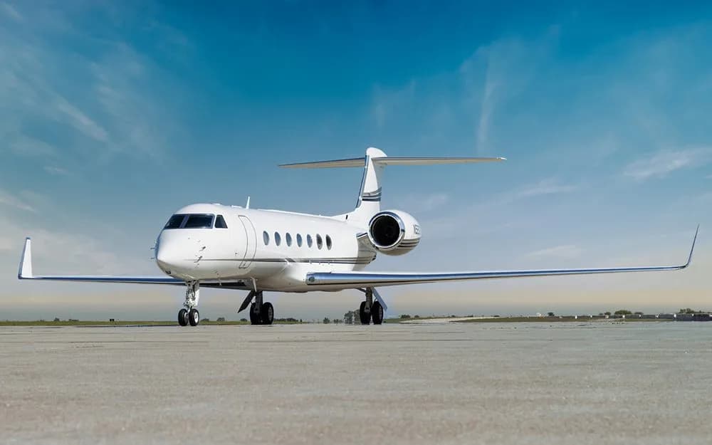 A white Gulfstream G550 business jet with a black stripe on the tail, viewed from the front on a tarmac.