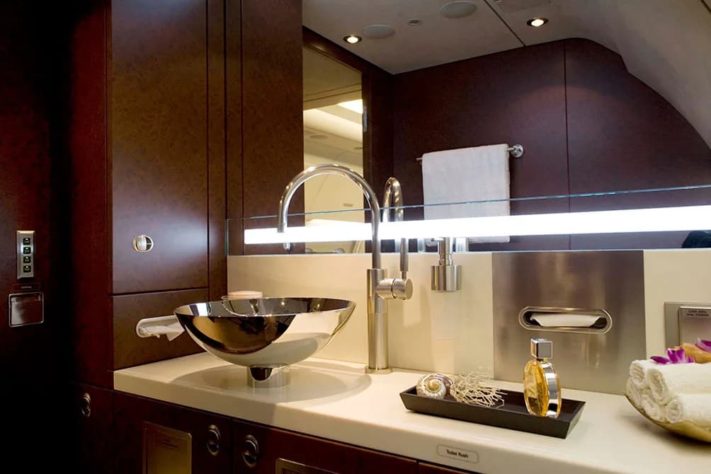 A luxurious private jet lavatory with a modern chrome sink, dark wood cabinetry, and elegant toiletries.