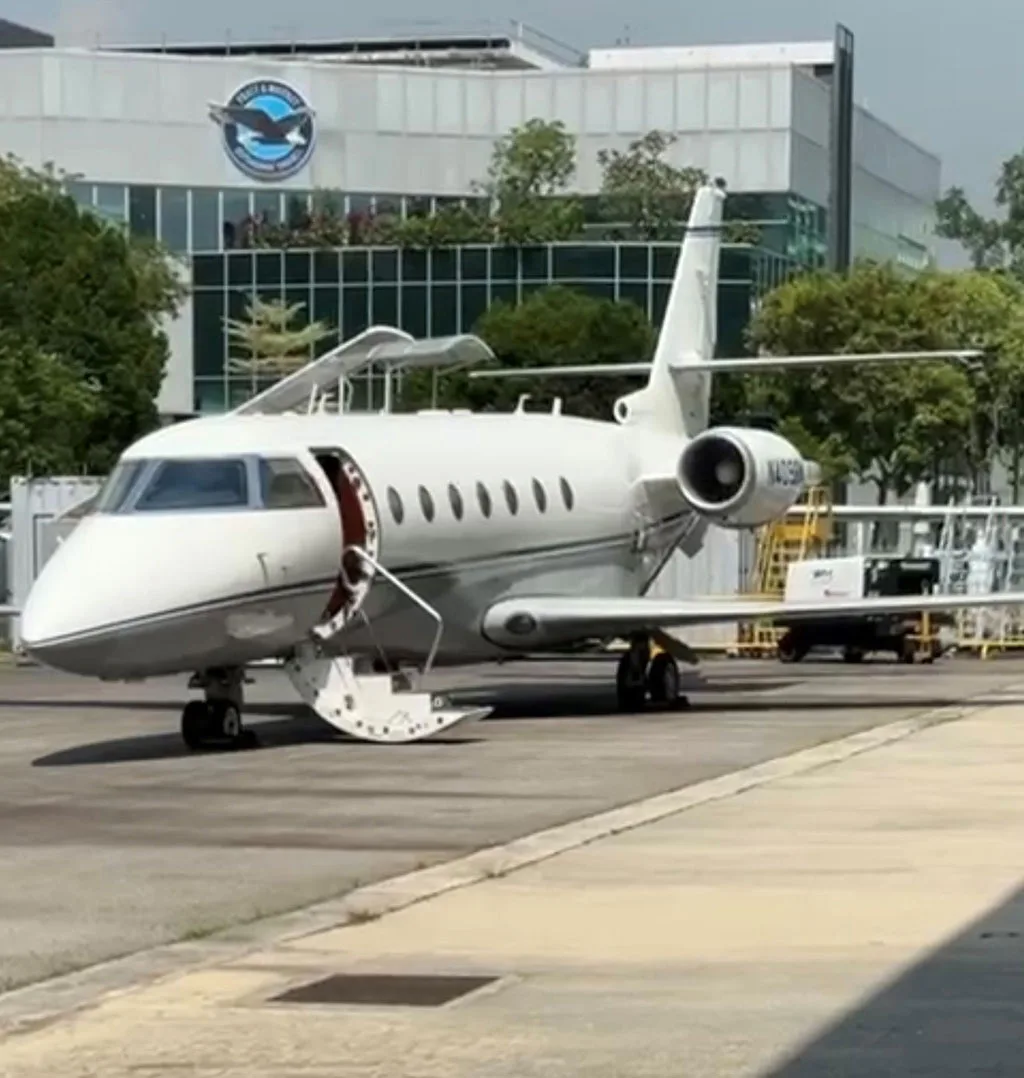 A white business jet, N409BM, with its main door open, parked on a tarmac in front of a modern building.