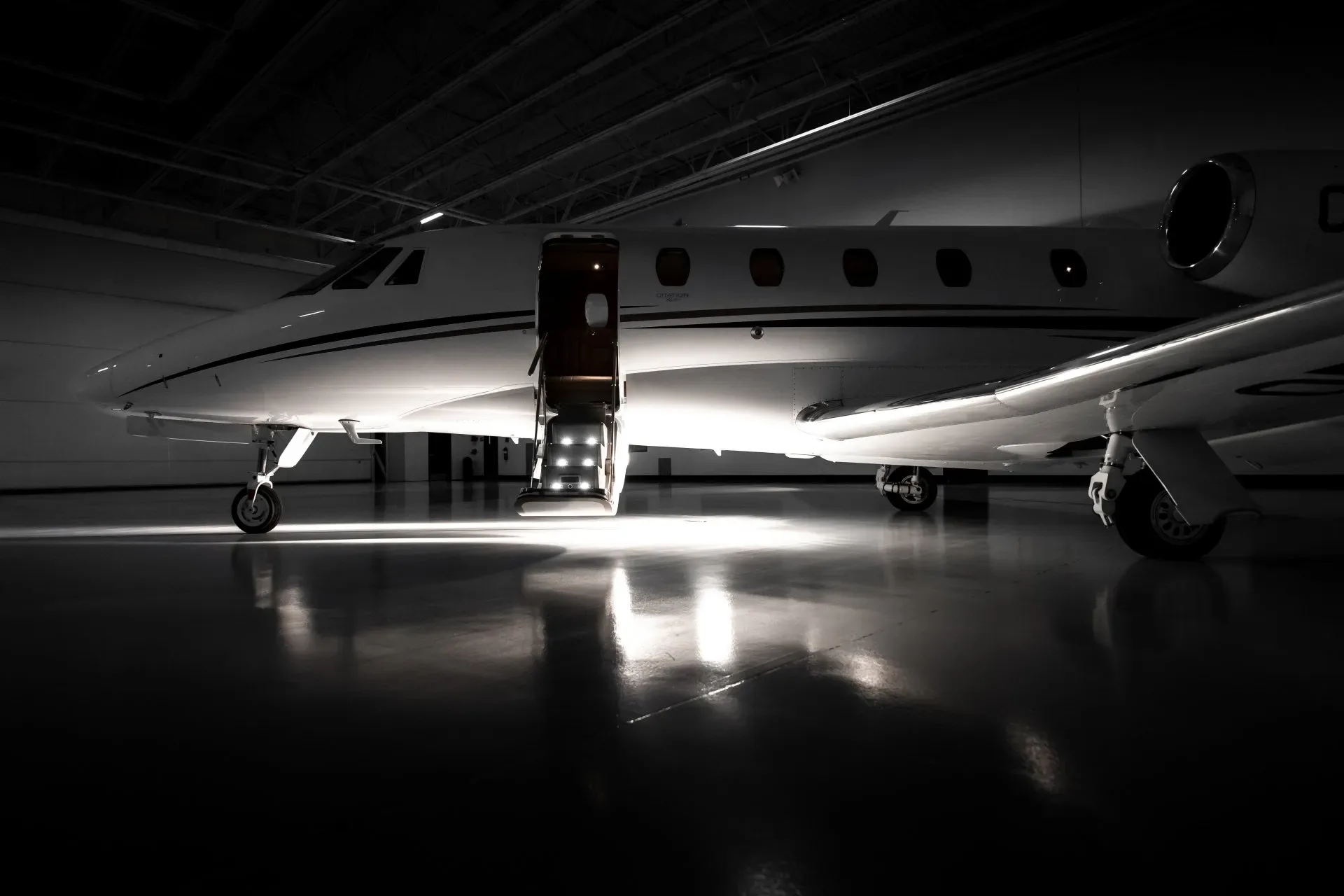 A white business jet is parked inside a hangar with the airstair door open.