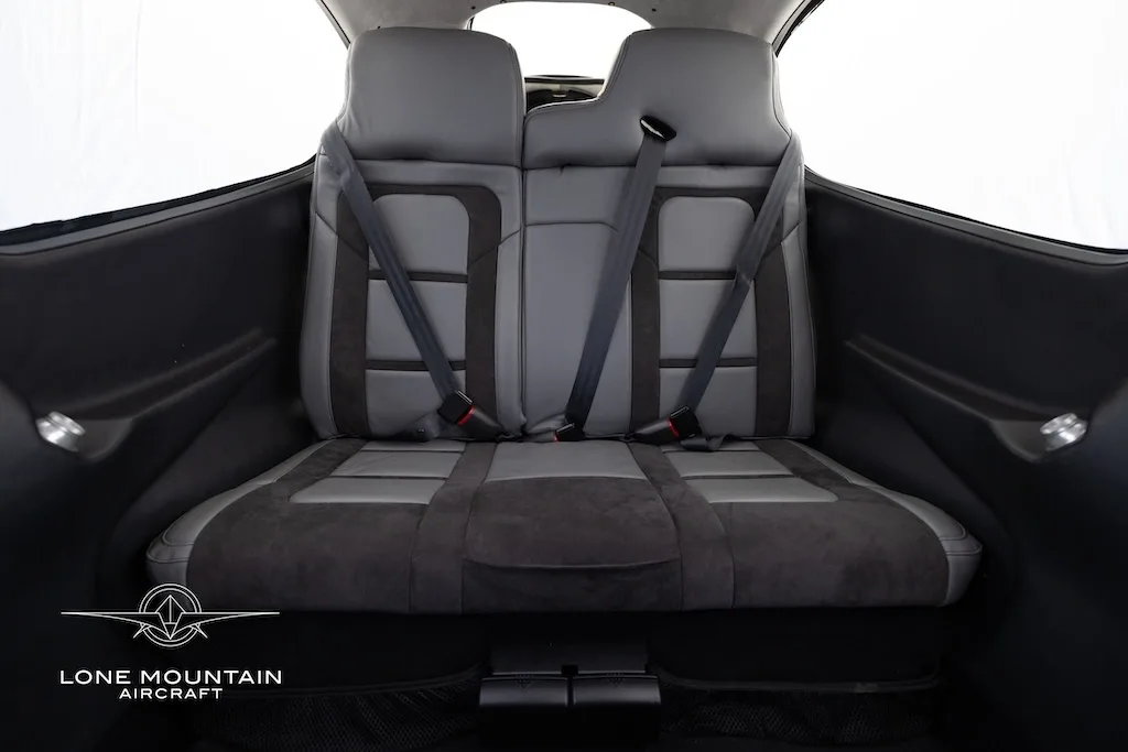 The grey and black rear passenger seats of the aircraft cabin with seatbelts fastened.