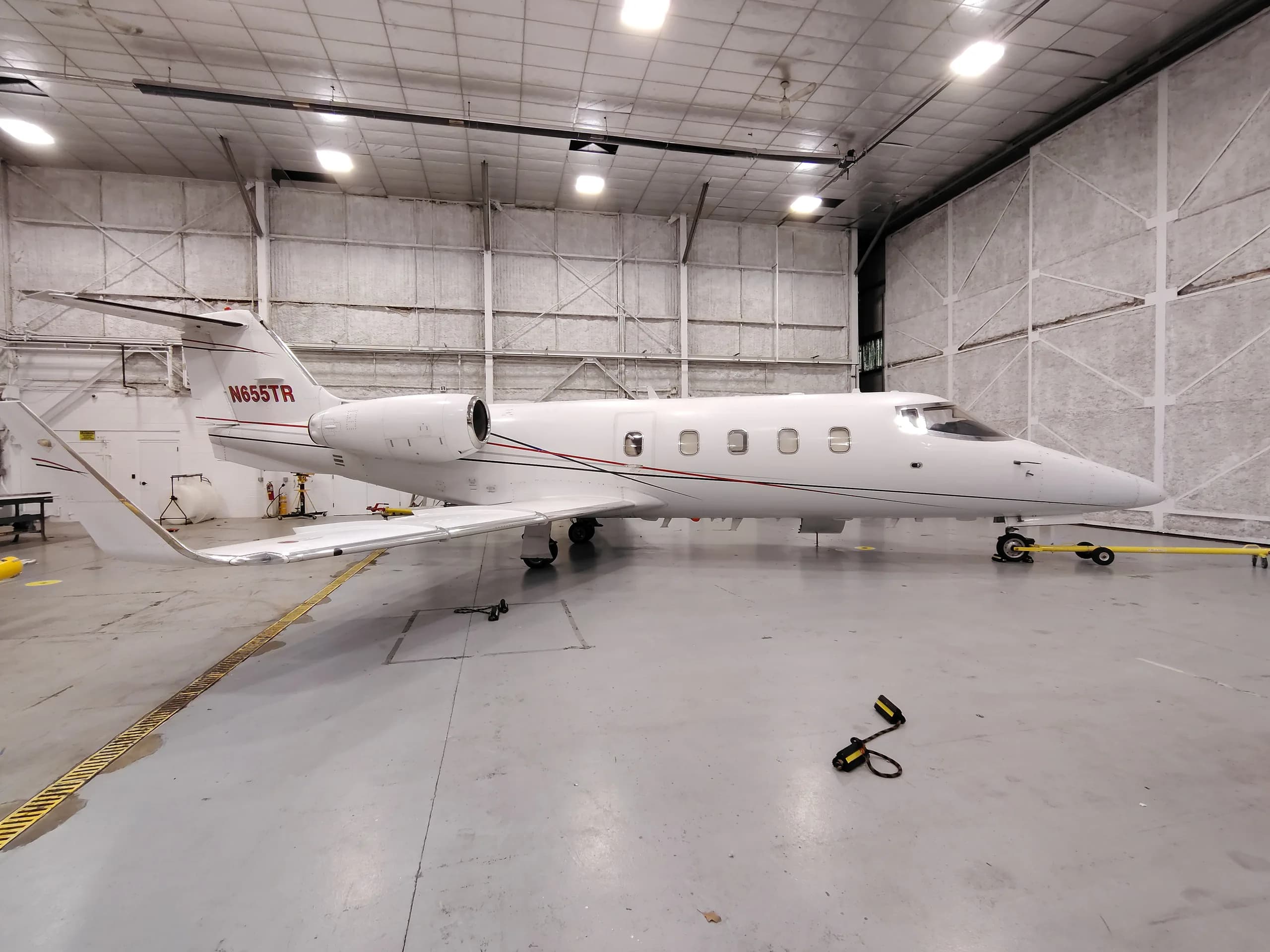 A white business jet with red and black stripes and registration N655TR is parked in a hangar.