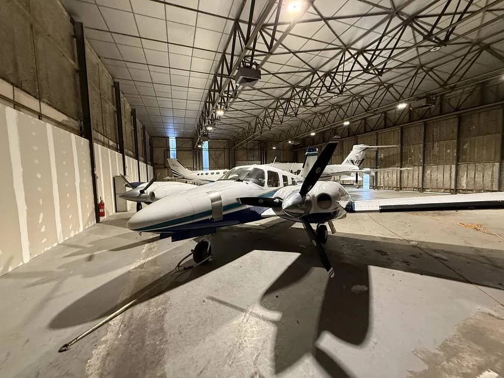 Front-left view of a white and blue Piper Seneca twin-engine propeller aircraft in a hangar.