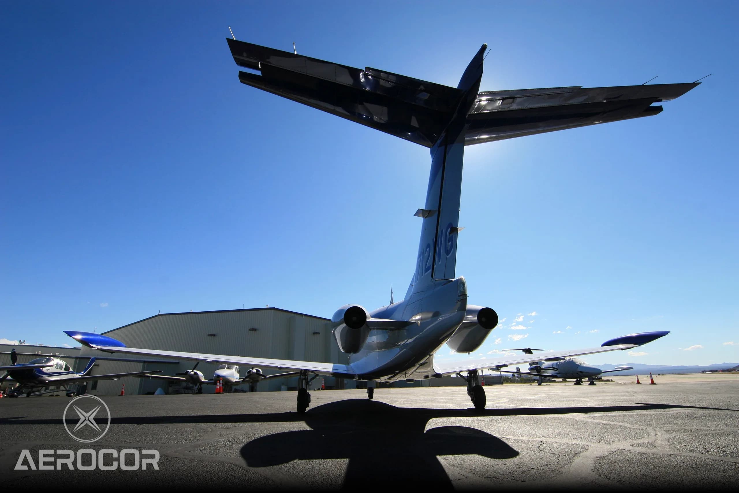 A rear view of the blue and white Eclipse 500/550 jet, N712WG, backlit by the sun on an airport tarmac.