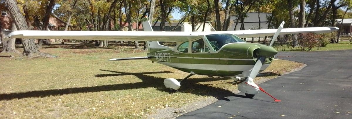 A Cessna aircraft with a green and white paint scheme is parked on the pavement.