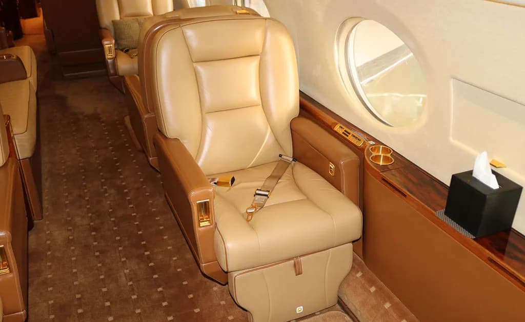 A single tan leather seat with a seatbelt and a small table extended from the side in a private jet cabin.