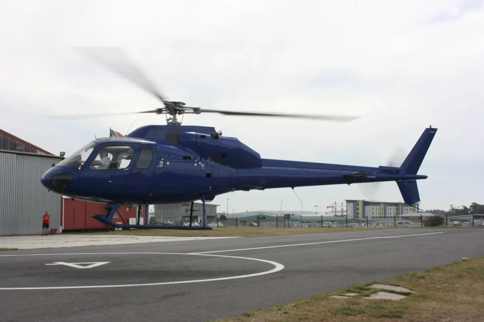 A blue helicopter on a helipad with its rotor blades spinning.