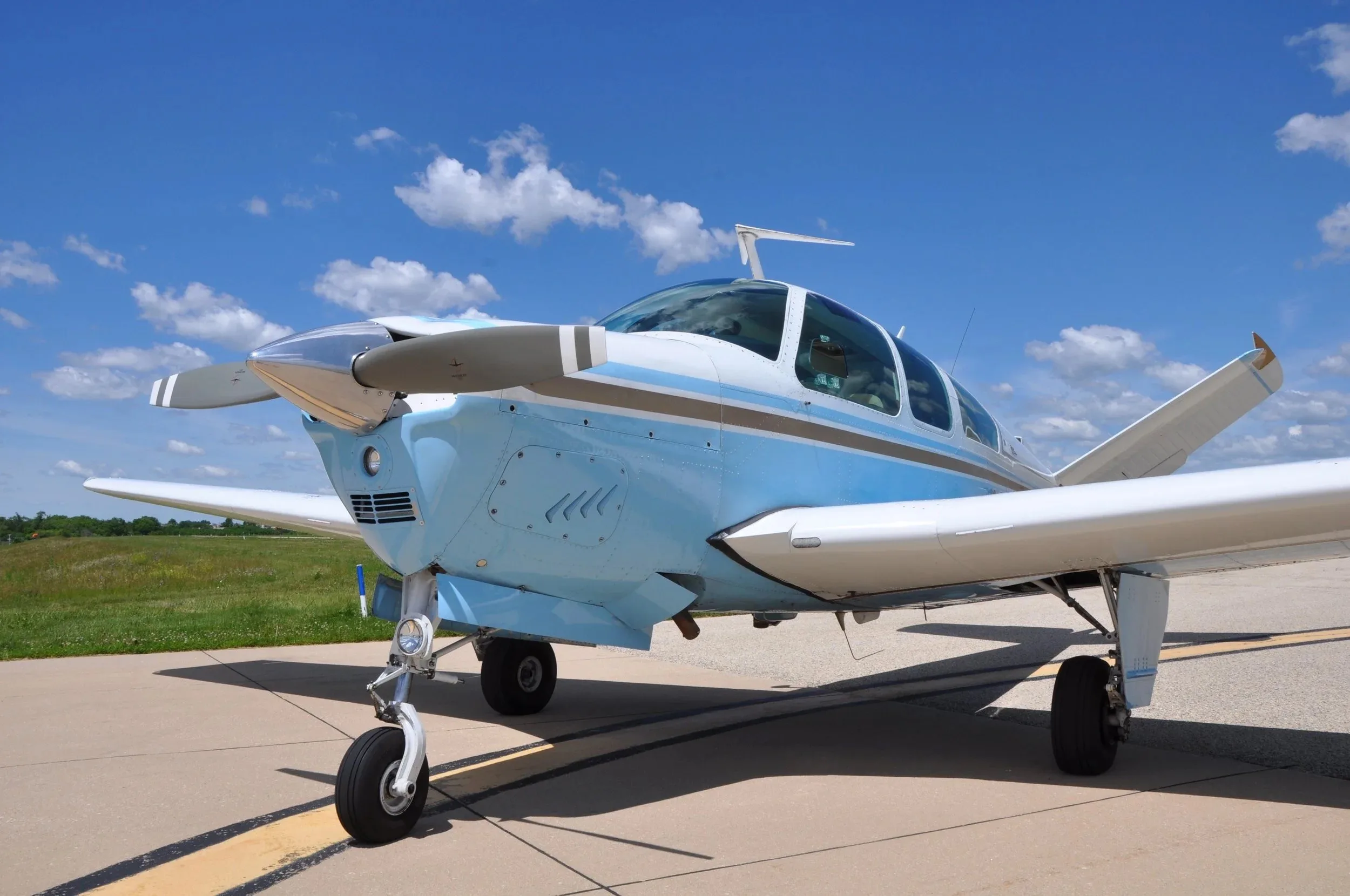 A front-side view of the light blue and white Beechcraft Bonanza N7128N on an airfield.