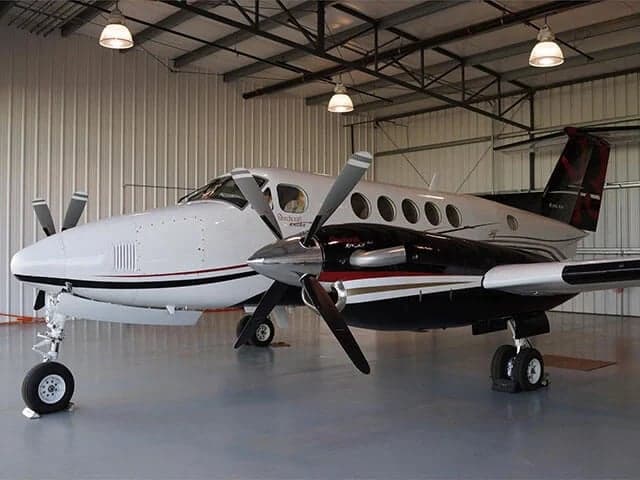 A white, black, and red Beechcraft King Air parked inside a well-lit hangar.