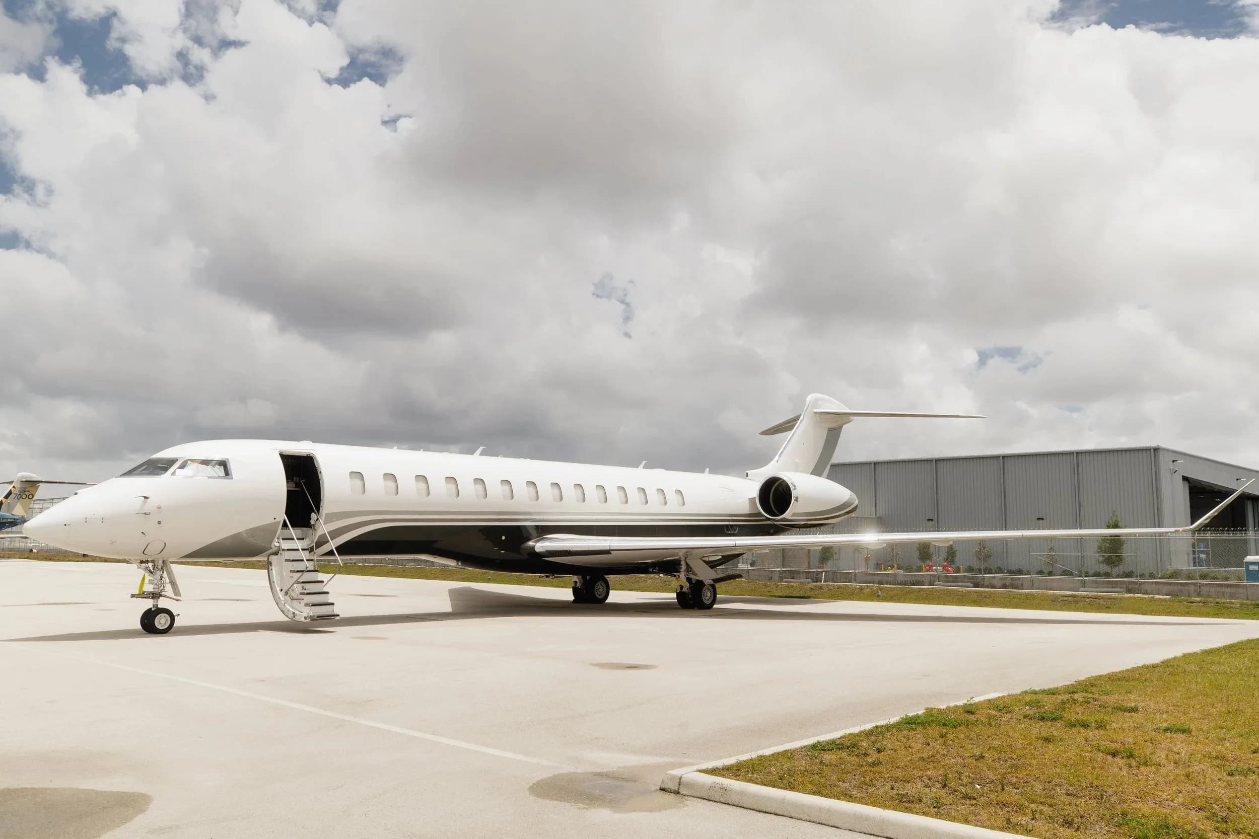 A white and grey Bombardier Global 7500 business jet is parked on an airfield with its main door open and stairs extended.