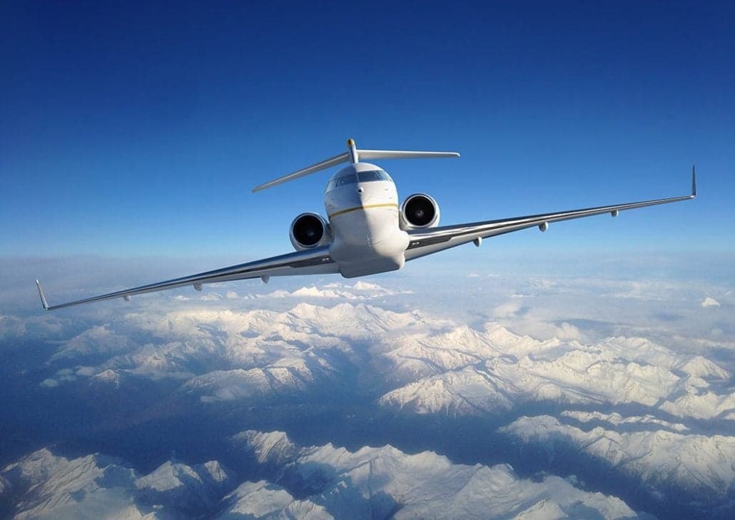 A Bombardier Global Express flying above snow-covered mountains.