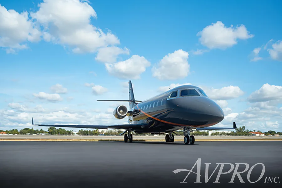 A frontal view of the Gulfstream G200 business jet, registration N119PS, with a dark gray and black paint scheme and orange accents, parked on an airfield.