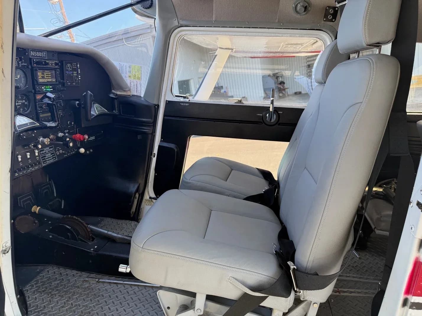 Cockpit and front cabin view of a light aircraft with grey seats and instrument panel.