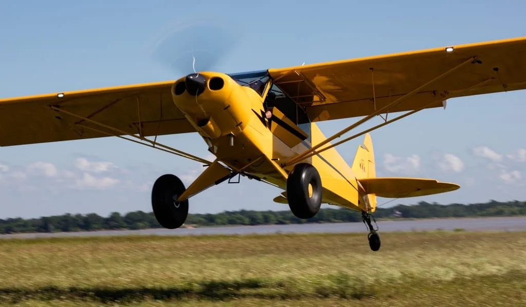 Yellow aircraft landing on a grassy field.