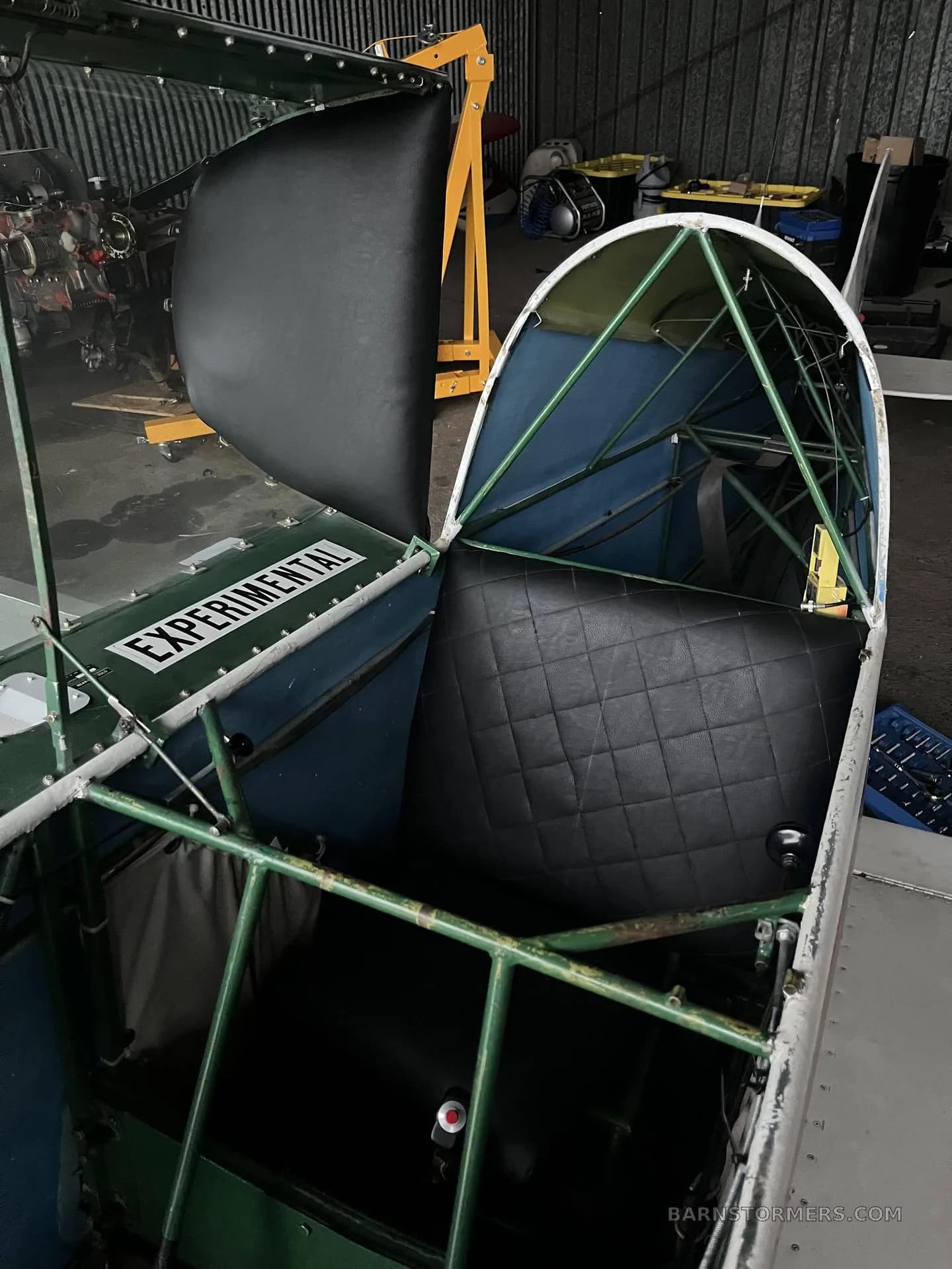 The interior of an experimental aircraft showing a black quilted seat and green structural tubing.