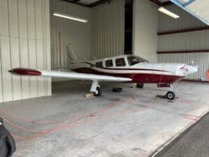 A maroon and white single-engine aircraft parked in a hangar.