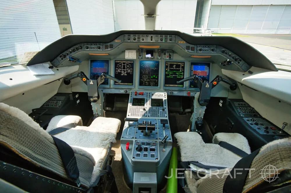 A wide-angle view of a modern aircraft cockpit with multiple digital displays and two pilot seats.