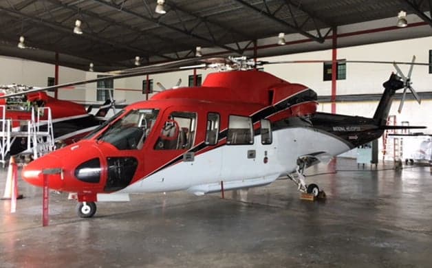 A red and white helicopter with "NATIONAL HELICOPTER" on the tail boom, parked in a hangar.