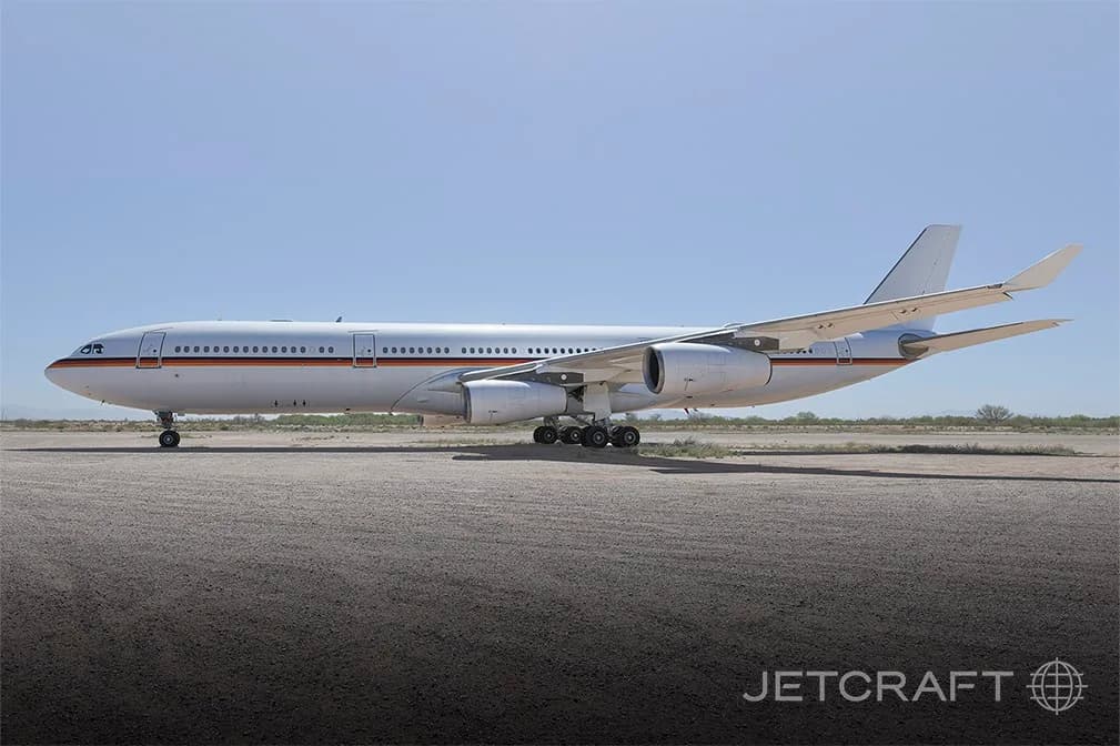 A side view of a white Airbus A340-300 with a German government livery parked on an airfield under a clear sky.