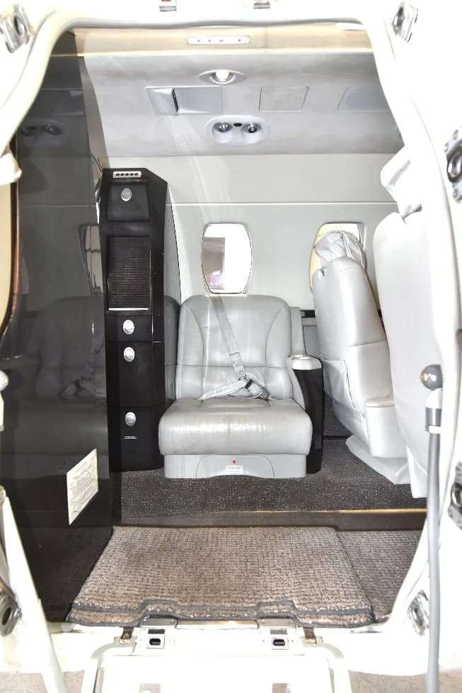 View from the open door into the private jet's cabin, showing a light gray seat and a dark storage cabinet.