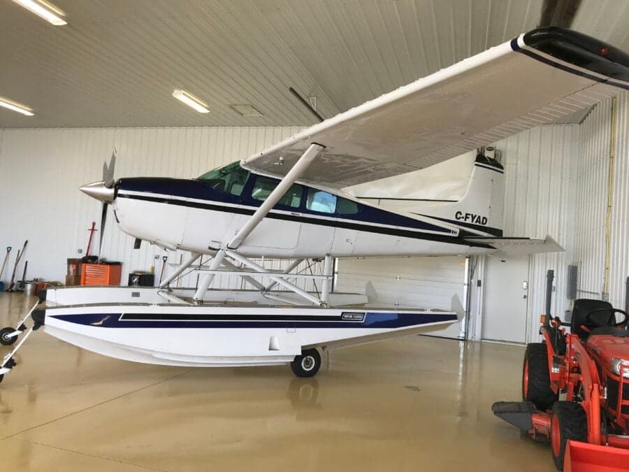 Side view of a white and blue Cessna on floats inside a hangar.