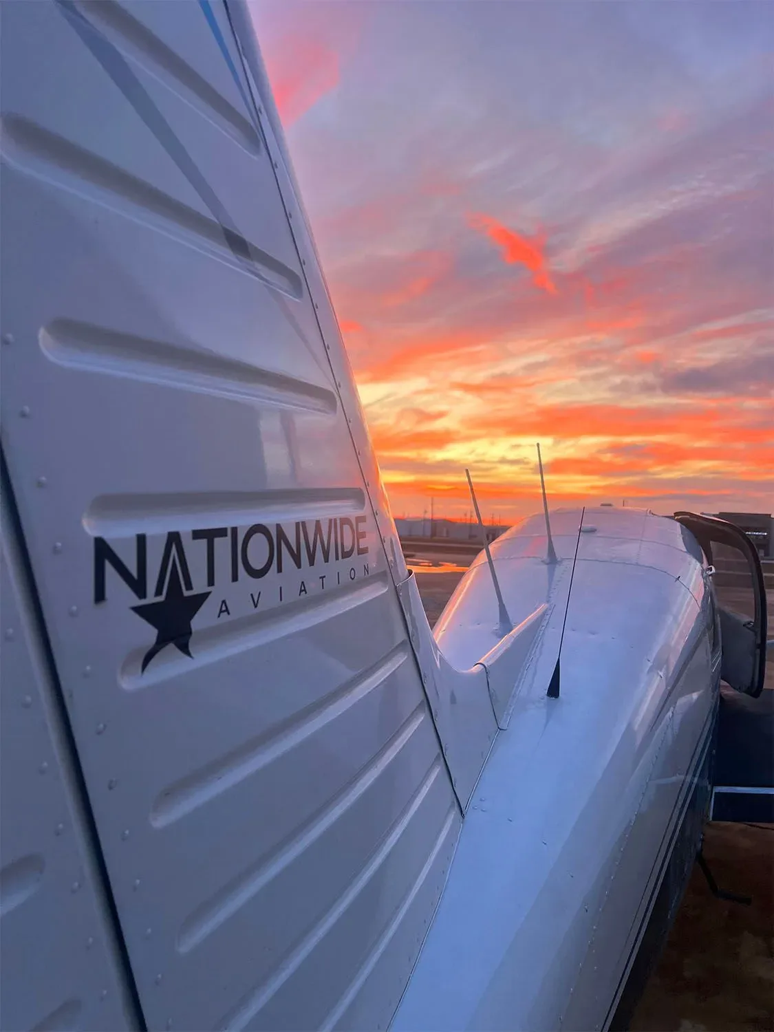 Tail section of an aircraft with the Nationwide Aviation logo against a colorful sunset sky.