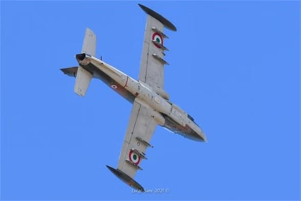 Camouflaged aircraft I-MBCK in flight against a blue sky.