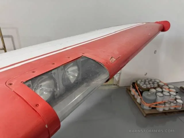 A close-up view of a red and white aircraft wingtip with landing lights, showing some wear.