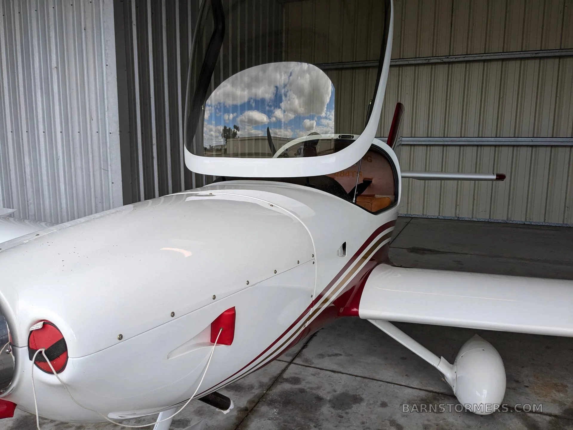 A close-up view of the front of a white and red aircraft with its canopy open, inside a hangar.