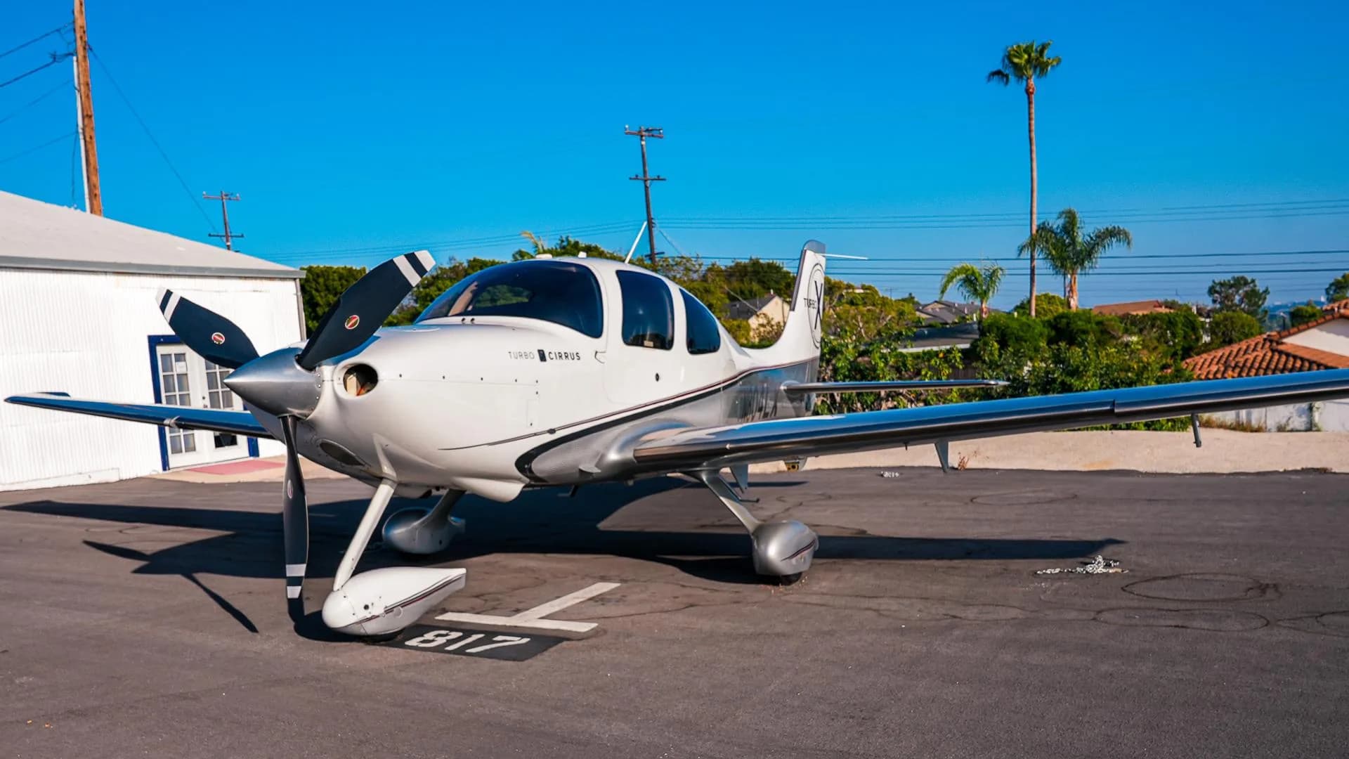 A white and silver Cirrus SR22T aircraft with a three-bladed propeller parked on an asphalt apron.