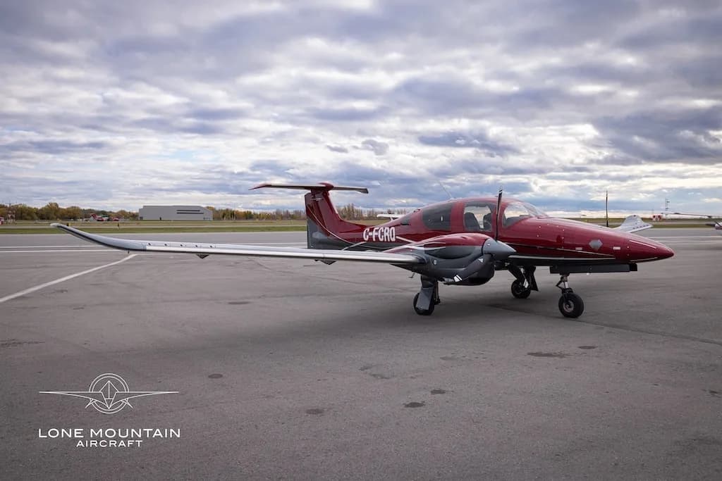 A red and grey Diamond DA62 aircraft with registration C-FCRQ parked on an airfield, viewed from the front-side.
