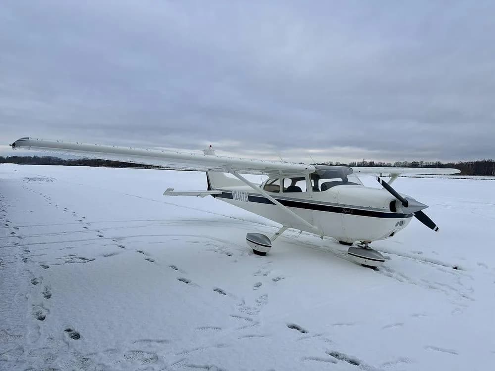 Front-left view of a white Cessna 172 N246TB with dark blue stripes, parked in the snow.