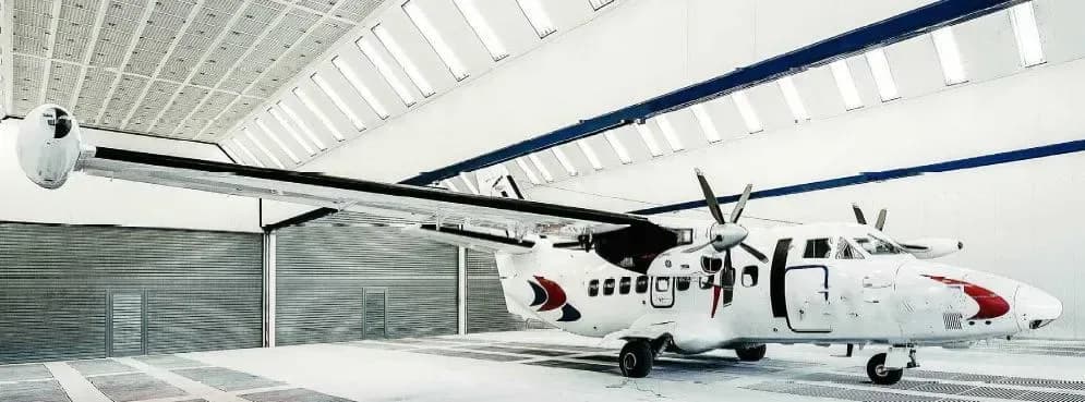 A white Let L-410 Turbolet aircraft is parked inside a hangar with its door open.
