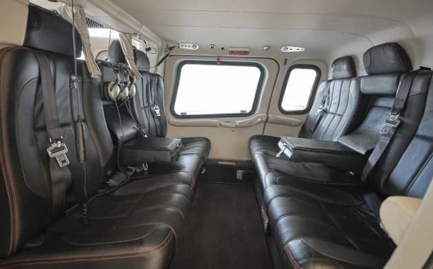 The helicopter's interior features black leather seats with red stitching and large windows.