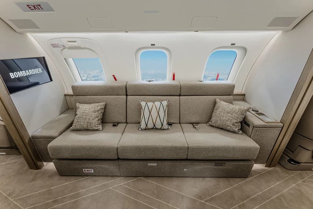A comfortable grey sofa with patterned pillows and a "Bombardier" screen in a private jet cabin.
