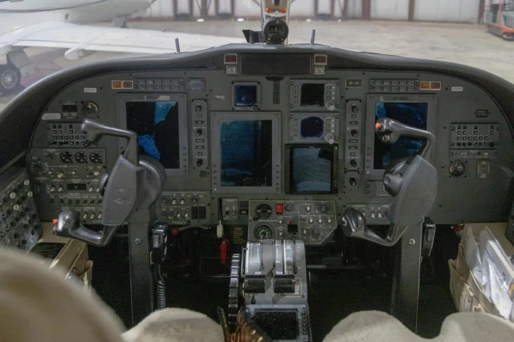 The cockpit of a business jet, showing the instrument panel with multiple screens and control yokes.